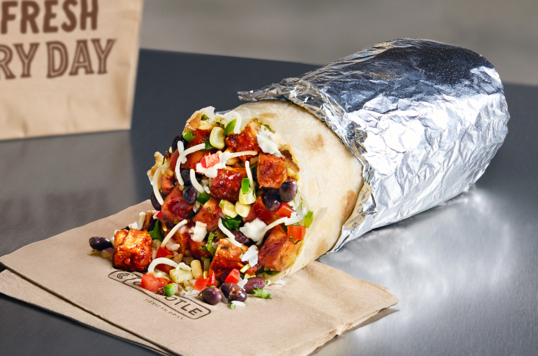 A close up point of view photo of a Chipotle Honey Chicken Burrito wrapped in foil and filled with white rice, black beans, freshly grilled Chipotle Honey Chicken, fresh tomato salsa, and roasted chili corn salsa.